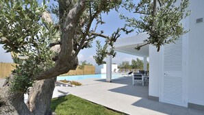 Zona d'una piscina moderna a l'aire lliure amb gandules, zona de seients coberta i un gran arbre.