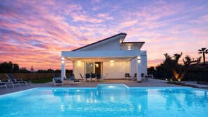 Una casa moderna amb piscina, mobiliari d'exterior i un cel al capvespre.