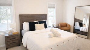 Ein Schlafzimmer mit einem großen Bett, einem Sessel, einem Nachttisch, einem Spiegel und einem Fenster.