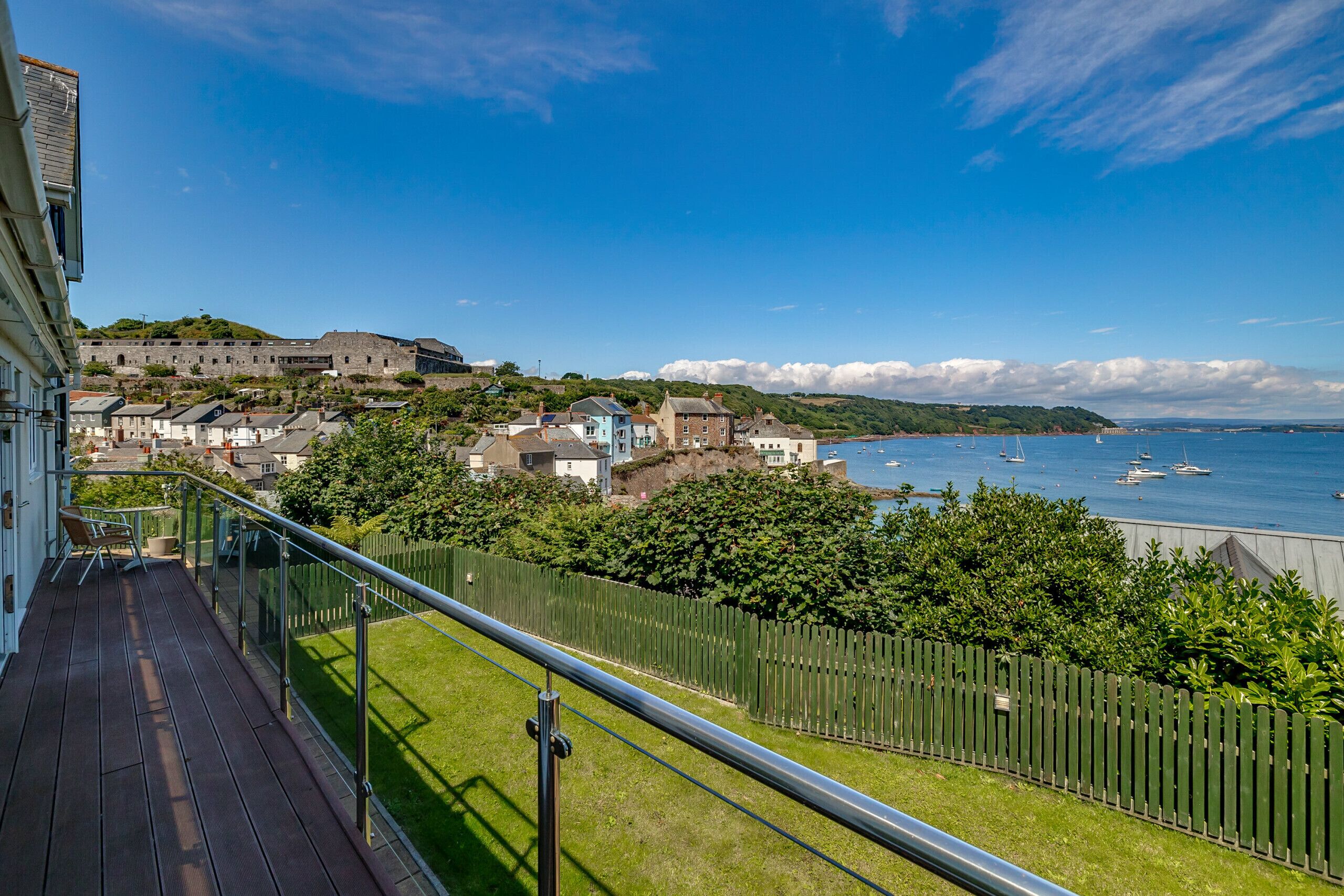 Un balcon offrant une vue sur une ville côtière, avec notamment un bâtiment historique et un ciel bleu dégagé.