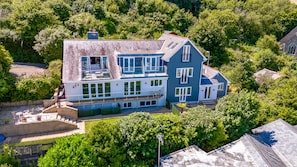 A large two-story house with multiple windows and balconies, surrounded by lush greenery.