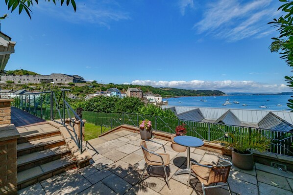 A patio with outdoor furniture, a view of the sea, and buildings in the background. - Bownder House (Cawsand)
