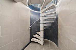 A spiral staircase with a modern design, surrounded by light-colored walls and a dark tiled floor.