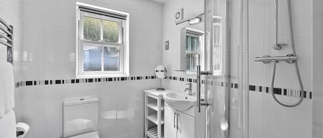A modern bathroom with a toilet, sink, and shower. There is a window above the toilet and a mirror above the sink.