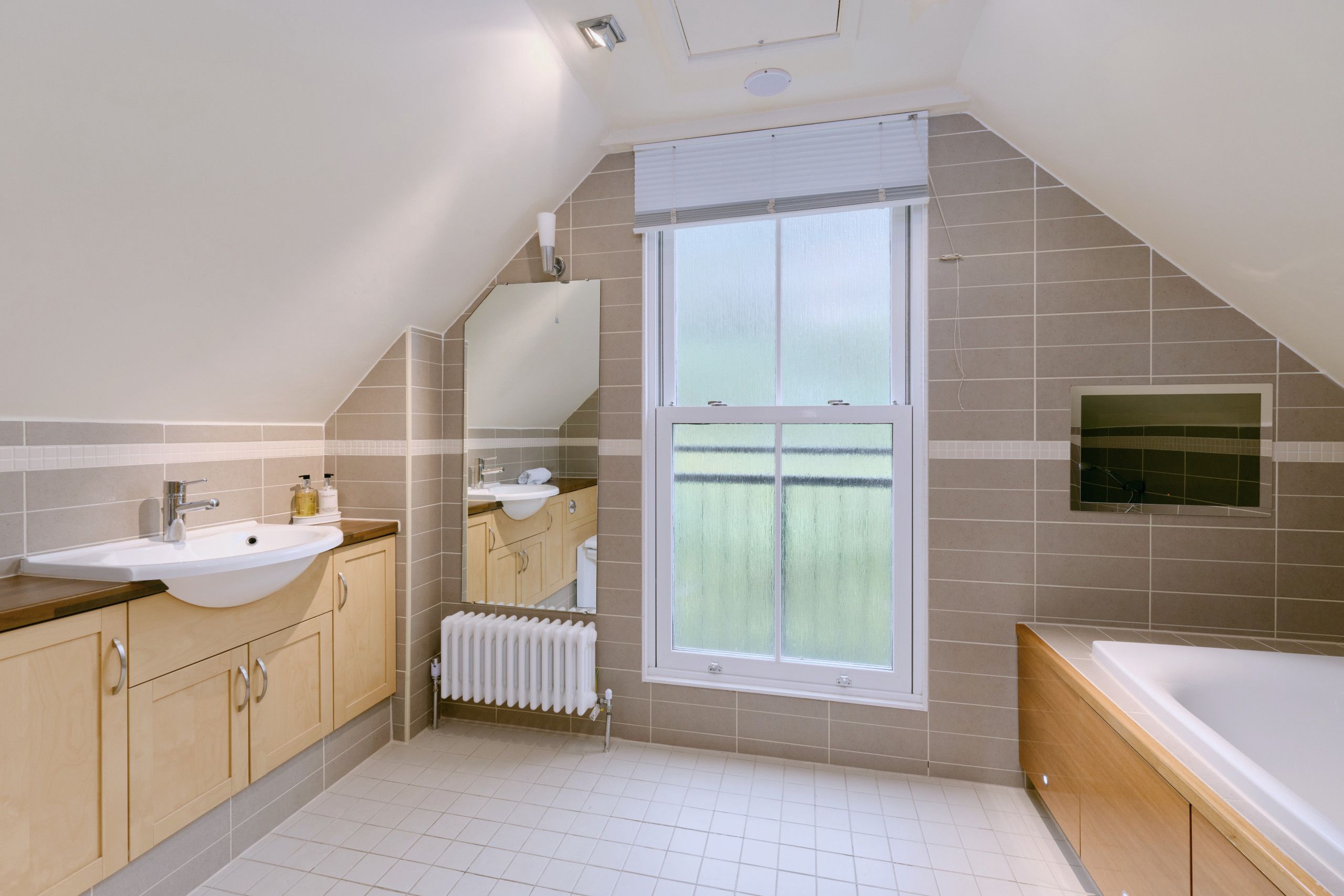 Ein modernes Badezimmer mit schrägverdeckelter Decke, einem großen Fenster und einer Badewanne.
