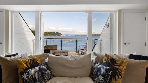 Een kamer met uitzicht op zee, een bank met kussens en een stoel.