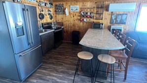 A kitchen with a stainless steel refrigerator, wooden cabinets, a granite countertop, and a bar area with stools. - Cozy 2-bedroom lakeside cabin with direct trail access (Ashland)