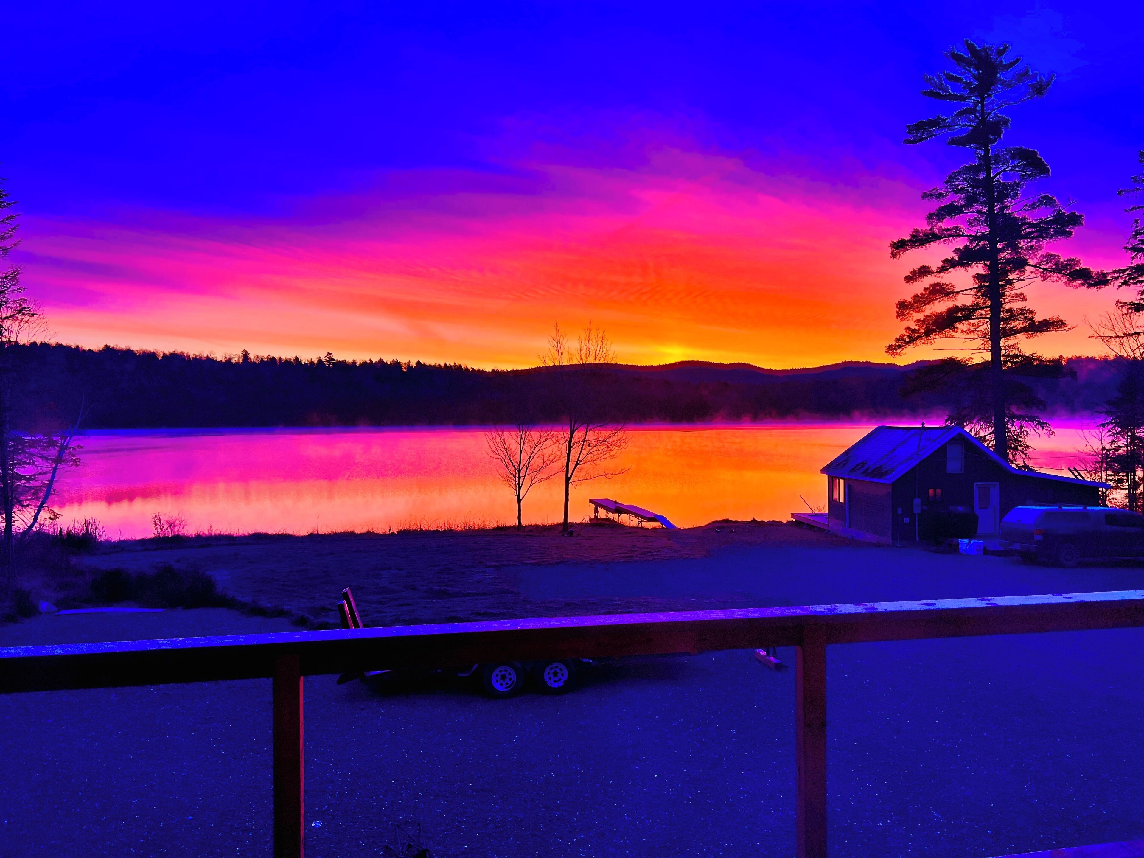 A cabin by a lake with a trailer in the foreground.