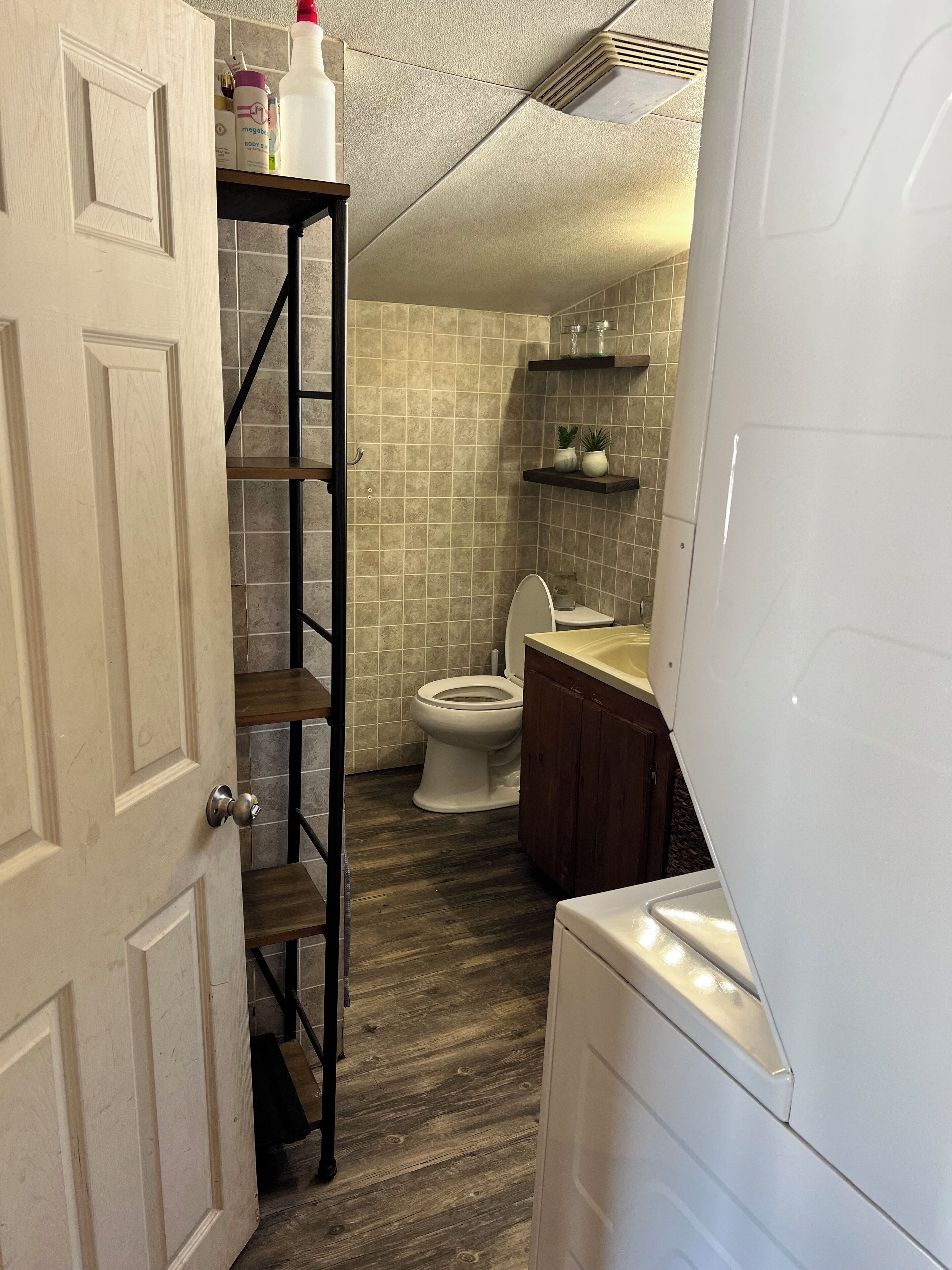 Une salle de bain avec des toilettes, une étagère contenant des articles de toilette et un plancher en bois.