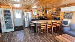 A cabin interior with a wooden ceiling, a kitchen area with a stove and refrigerator, a dining table with chairs, and a sofa. - Cozy 2-bedroom lakeside cabin with direct trail access (Ashland)