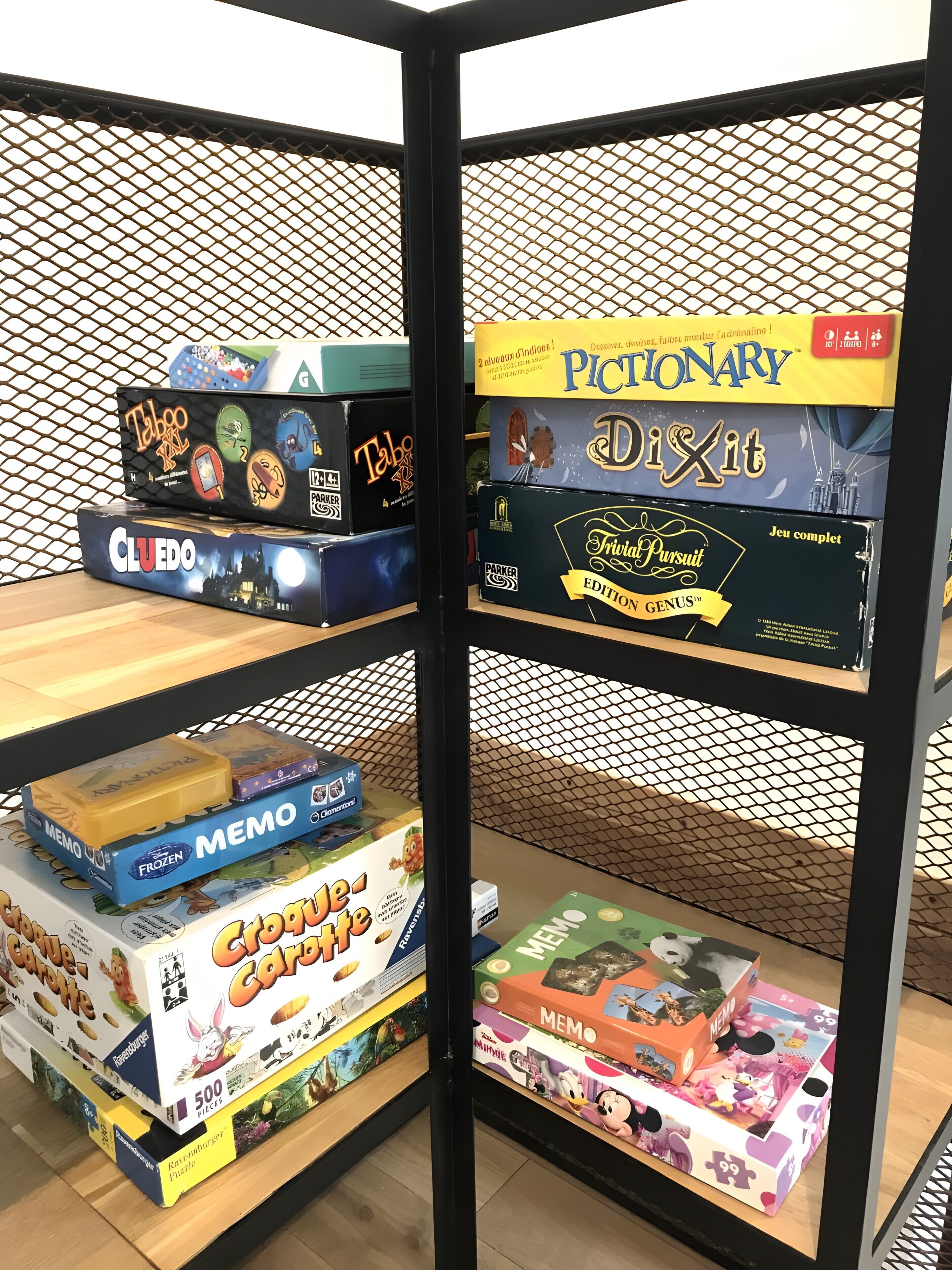 Une exposition de jeux de société présentée sur des étagères, avec un fond en treillis métallique.