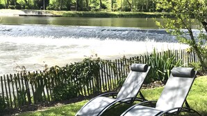 Un cadre paisible au bord d’un lac, avec une jetée en bois, un petit bateau et deux chaises longues donnant sur l’eau.