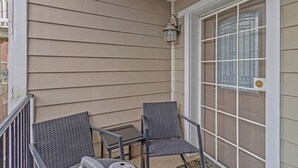 Eine überdachte Veranda mit beiger Fassade, eine Glastür mit Fenster und zwei Korbstühle mit einem kleinen Tisch.