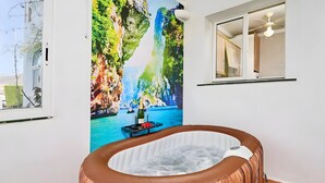 Quarto com banheira de madeira, um grande mural de uma cascata e janela com vista para um edifício.