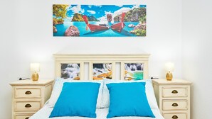 Quarto com cama, duas mesas de cabeceira, um quadro pendurado na parede e uma luminária em cada mesa de cabeceira.