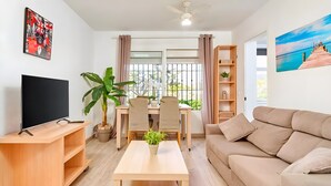 Uma sala de estar com televisão, sofá, mesa, cadeiras e uma planta.