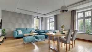 A modern living room with a blue sofa set, a wooden dining table with chairs, and large windows with curtains. - Tobiasza by Browar Hevelius Apartments (Gdańsk)