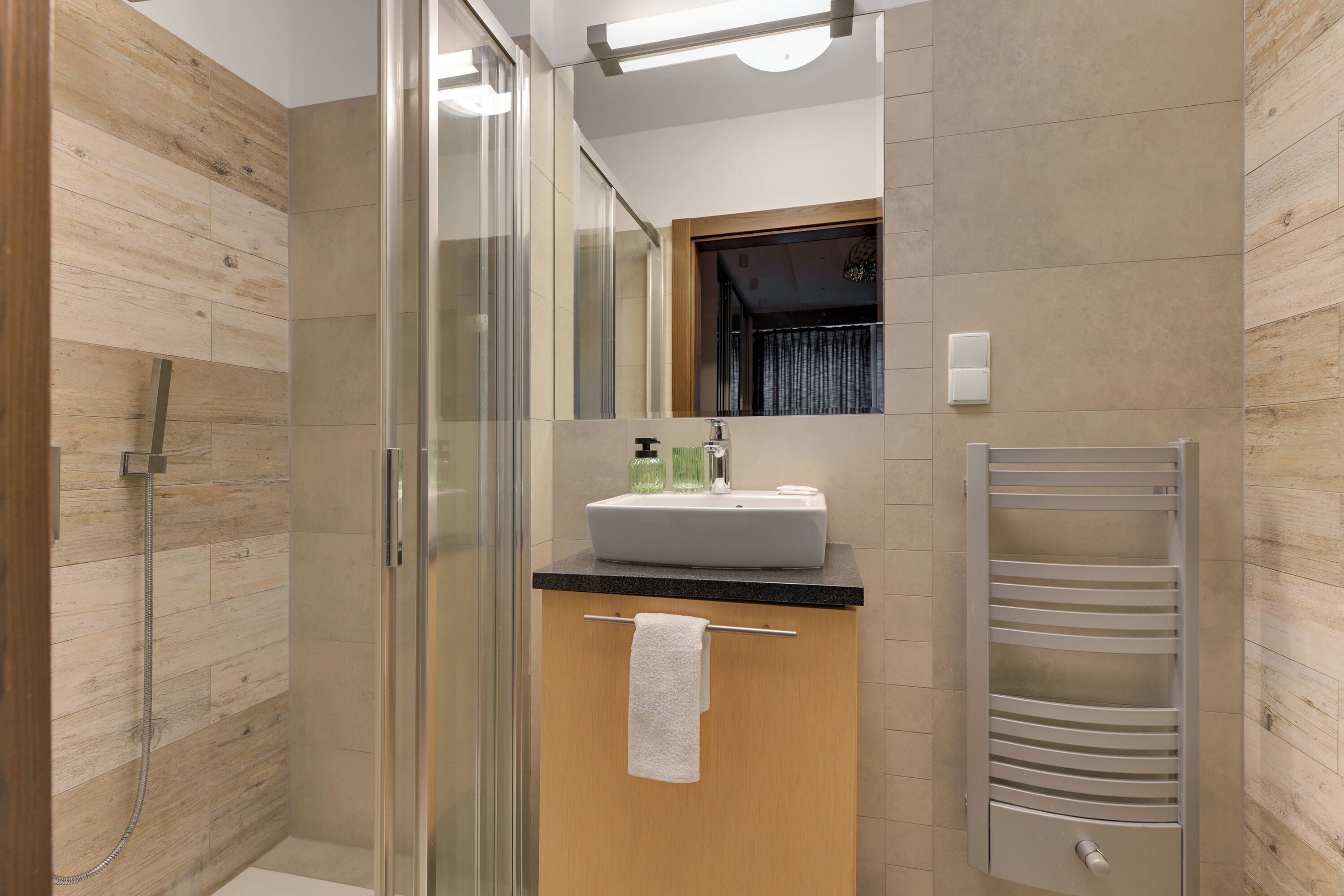 Un baño moderno con cabina de ducha de vidrio, tocador de madera con lavamanos y un perchero para toallas.