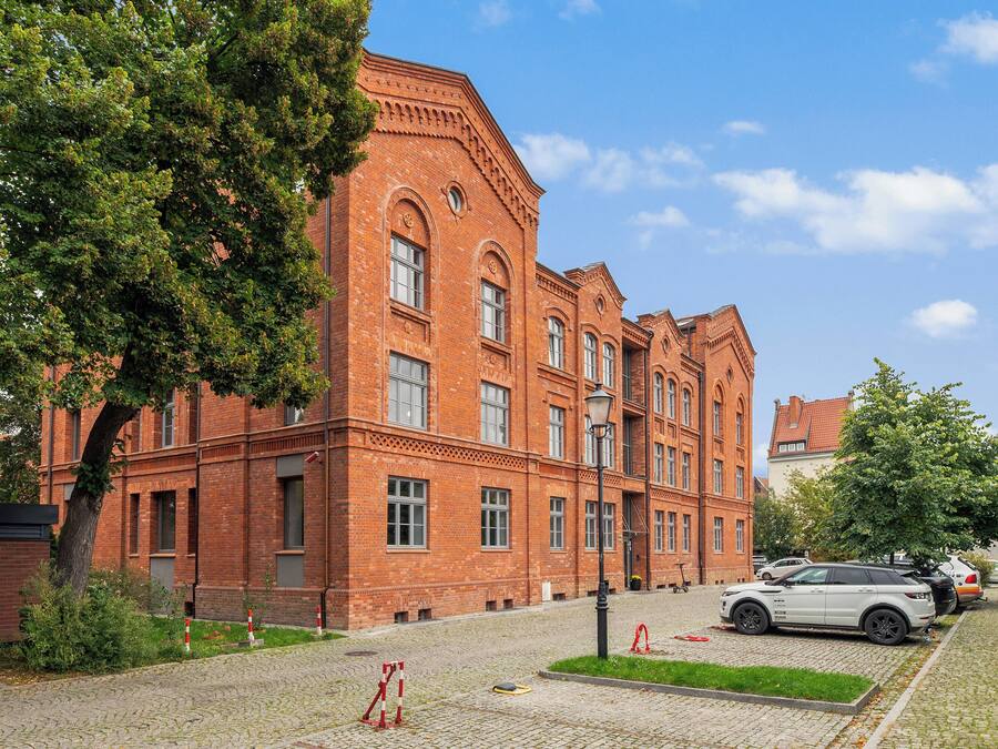 Ein rot backsteiner Gebäude mit vielen Fenstern und einer gepflasterten Auffahrt.