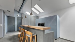 A modern kitchen with a central island, bar stools, pendant lighting, and built-in appliances. - Tobiasza by Browar Hevelius Apartments (Gdańsk)