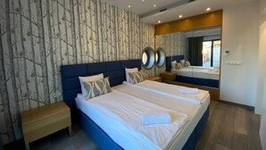 A modern hotel room with a large bed, a bench, a mirror, and a wall with a tree pattern. - Tobiasza by Browar Hevelius Apartments (Gdańsk)