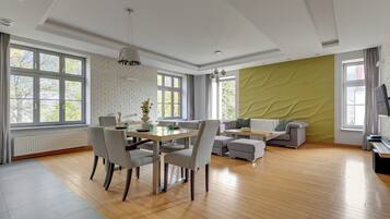 A spacious living room with a dining area, large windows, and a green accent wall.