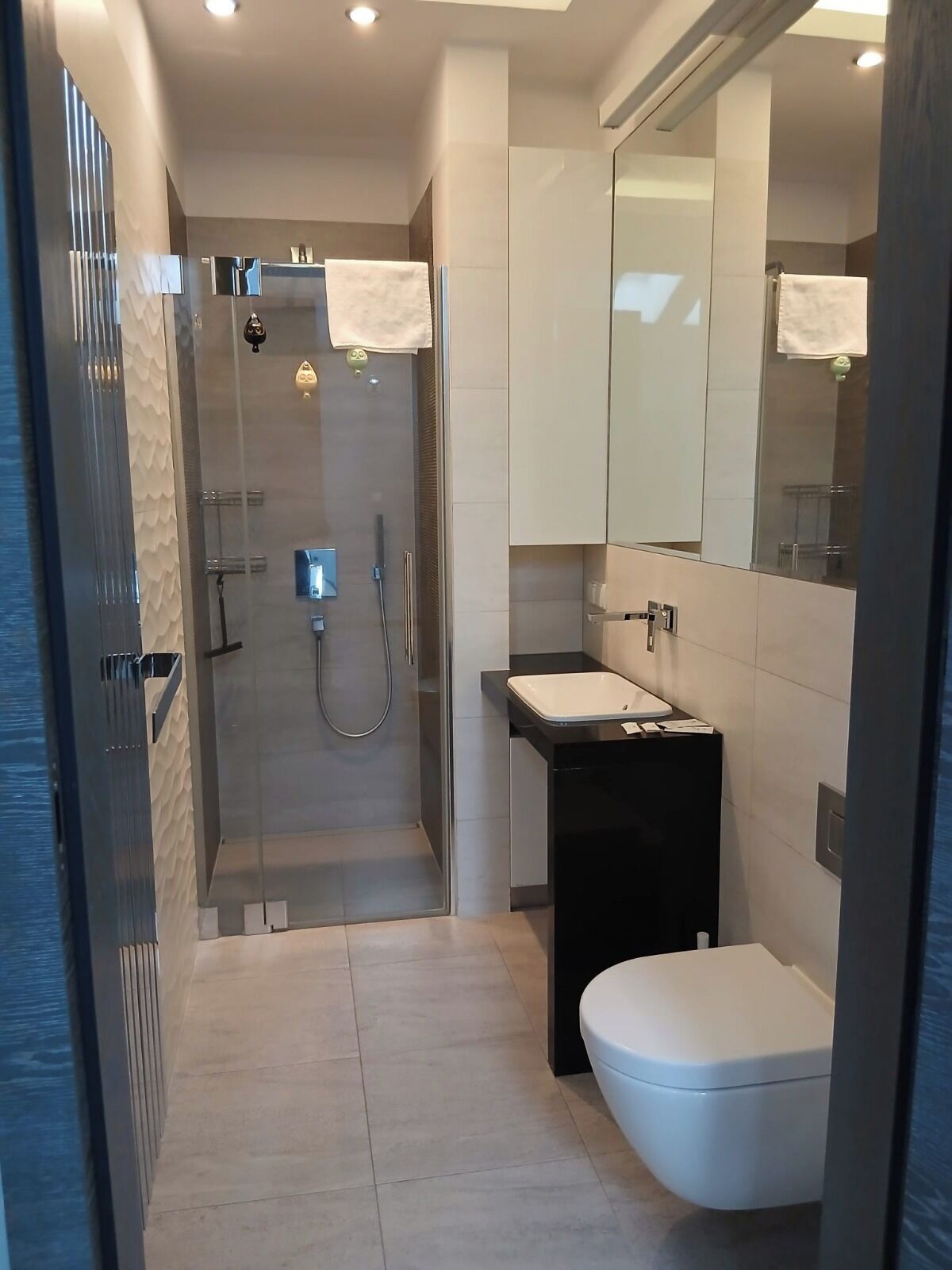 A modern bathroom with a glass-enclosed shower, a black sink, and a white toilet.