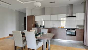A modern kitchen with grey cabinets, a built-in oven, and a dining area with a wooden table and grey chairs.