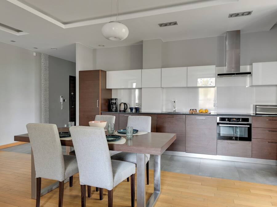A modern kitchen with grey cabinets, a built-in oven, and a dining area with a wooden table and grey chairs.