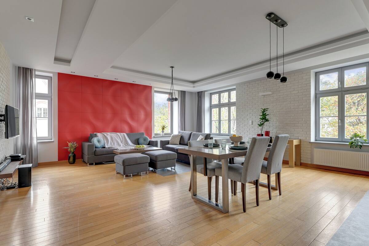 A spacious living area with a dining table, grey sofas, and a red accent wall.