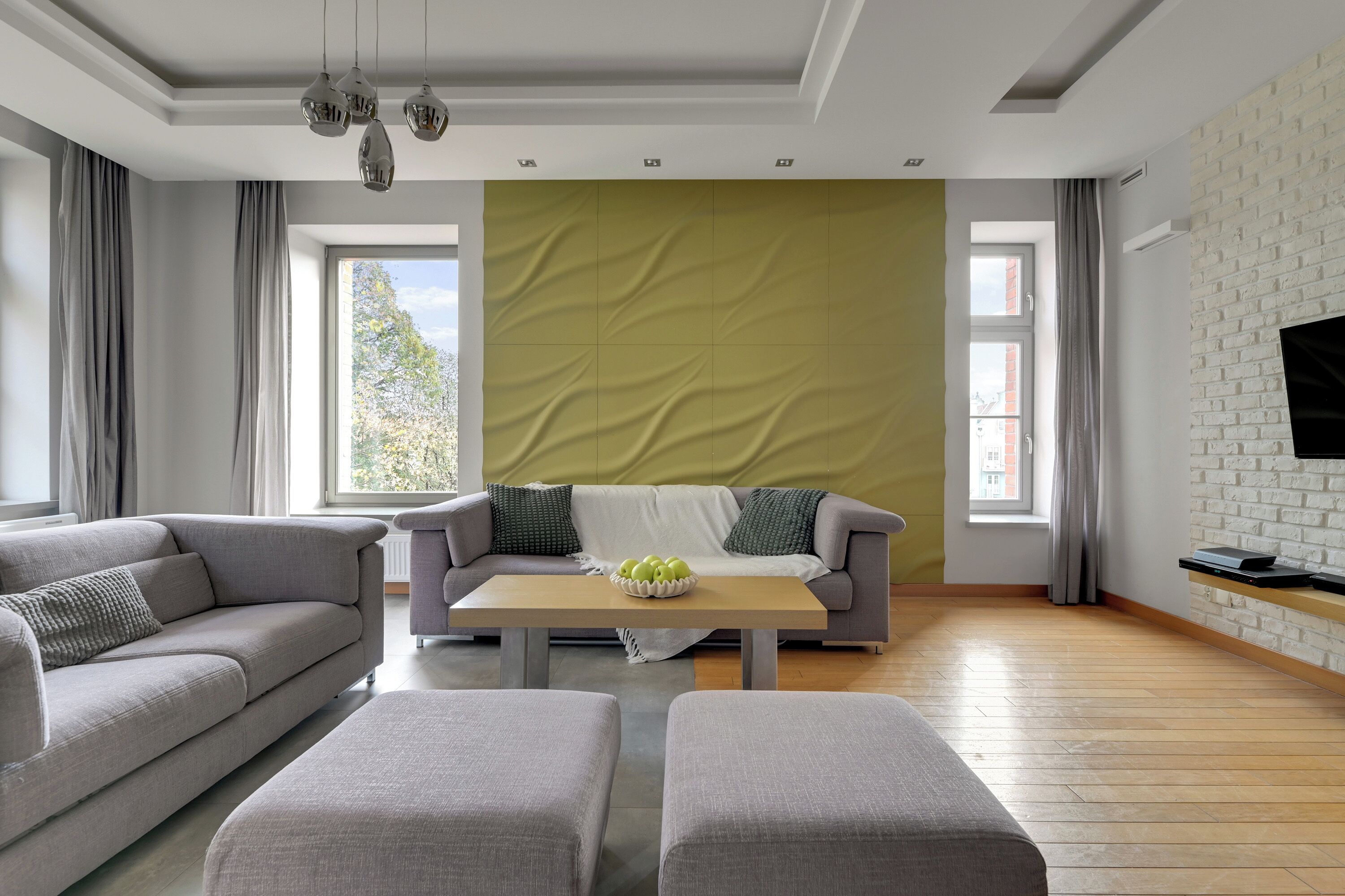 A modern living room with a sofa, ottoman, and a coffee table with apples.