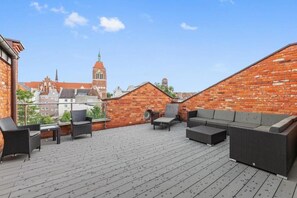 A rooftop terrace with wicker furniture, a brick wall, and a view of a church tower. - Tobiasza by Browar Hevelius Apartments (Gdańsk)