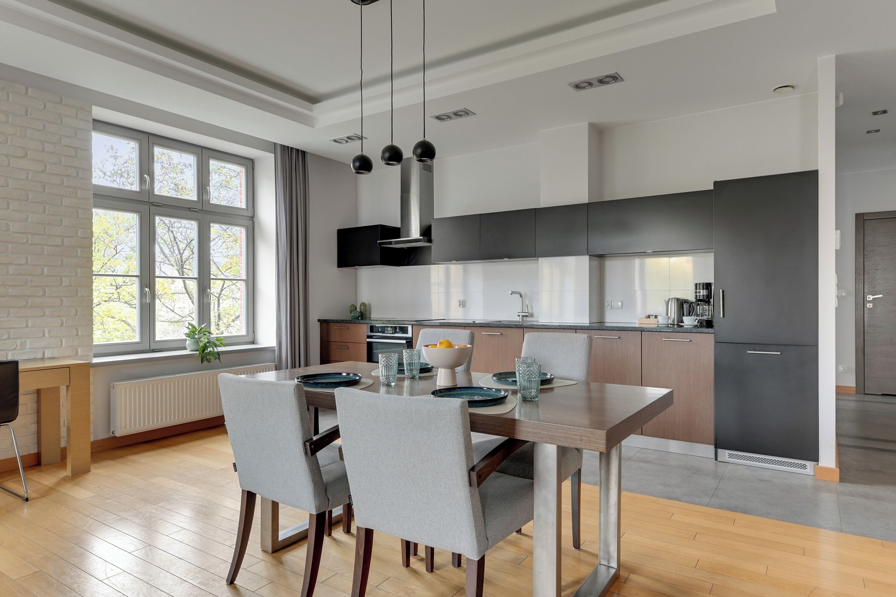A modern kitchen with a dining area, featuring a large window, built-in appliances, and a clean, minimalist design.