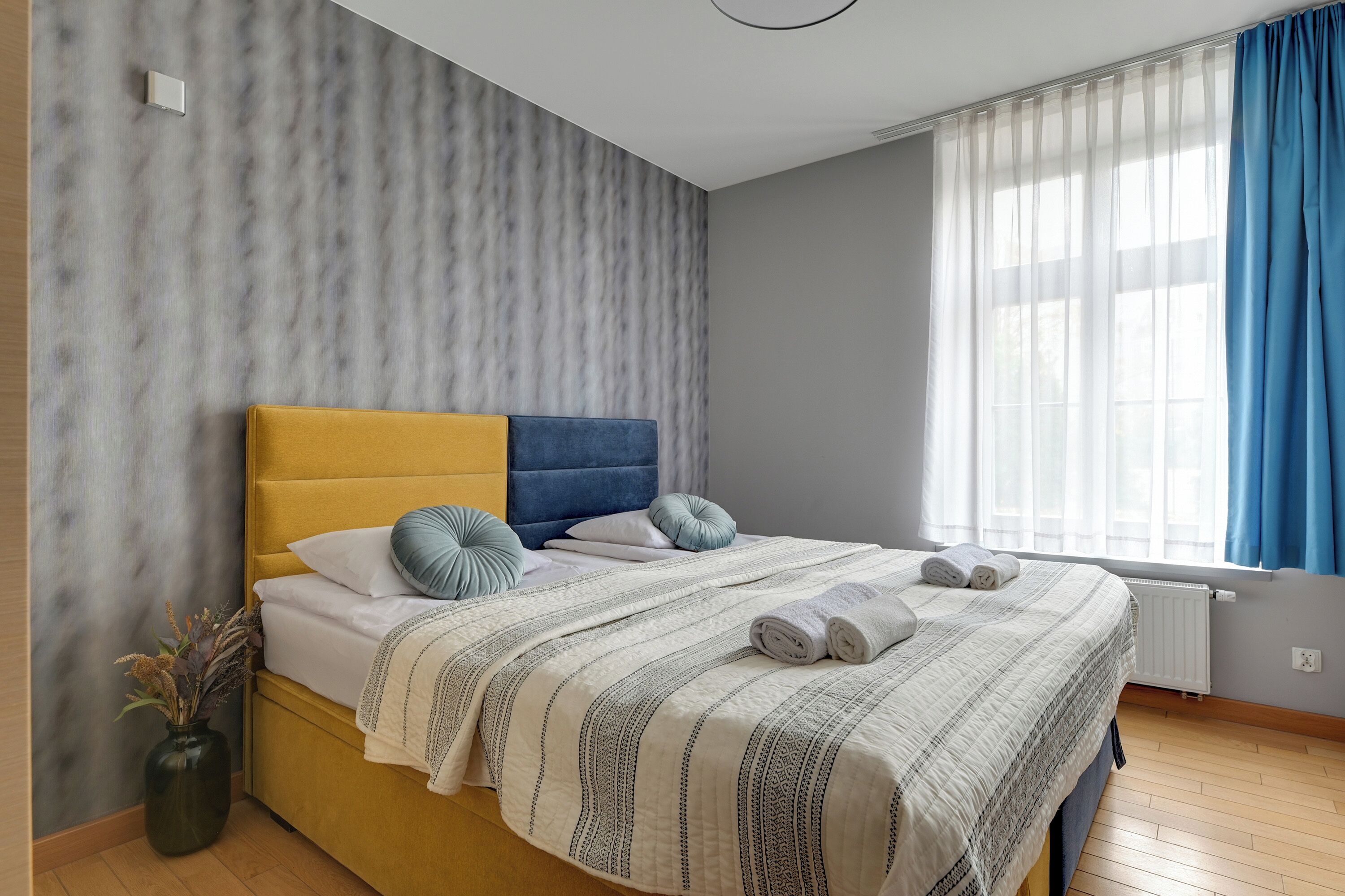 Una camera da letto moderna con un letto, un vaso con piante essiccate e una finestra con tende.
