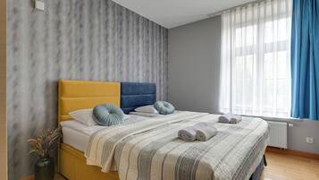 Une chambre à coucher moderne avec un lit, un vase contenant des plantes séchées et une fenêtre avec des rideaux.