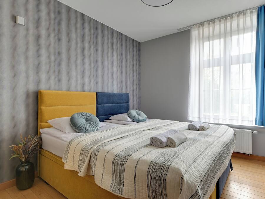 Une chambre à coucher moderne avec un lit, un vase contenant des plantes séchées et une fenêtre avec des rideaux.