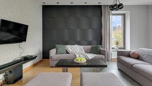 A modern living room with a flat-screen TV, a sofa, a coffee table, and a large window with a view of buildings. - Tobiasza by Browar Hevelius Apartments (Gdańsk)