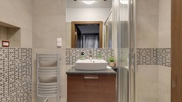 A modern bathroom with a large sink, a glass shower enclosure, and a patterned tile backsplash.