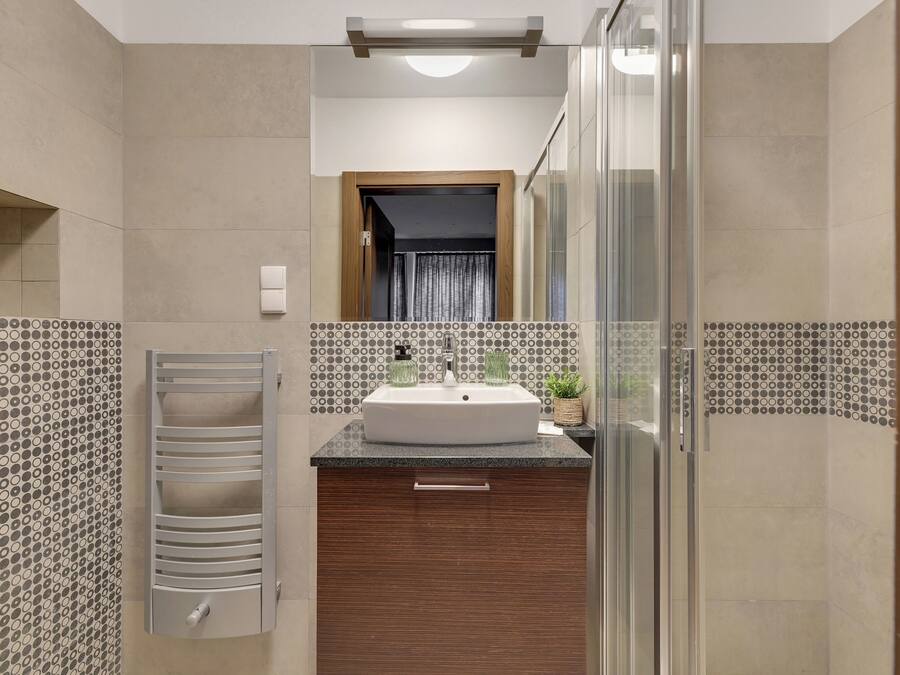 A modern bathroom with a large sink, a glass shower enclosure, and a patterned tile backsplash.