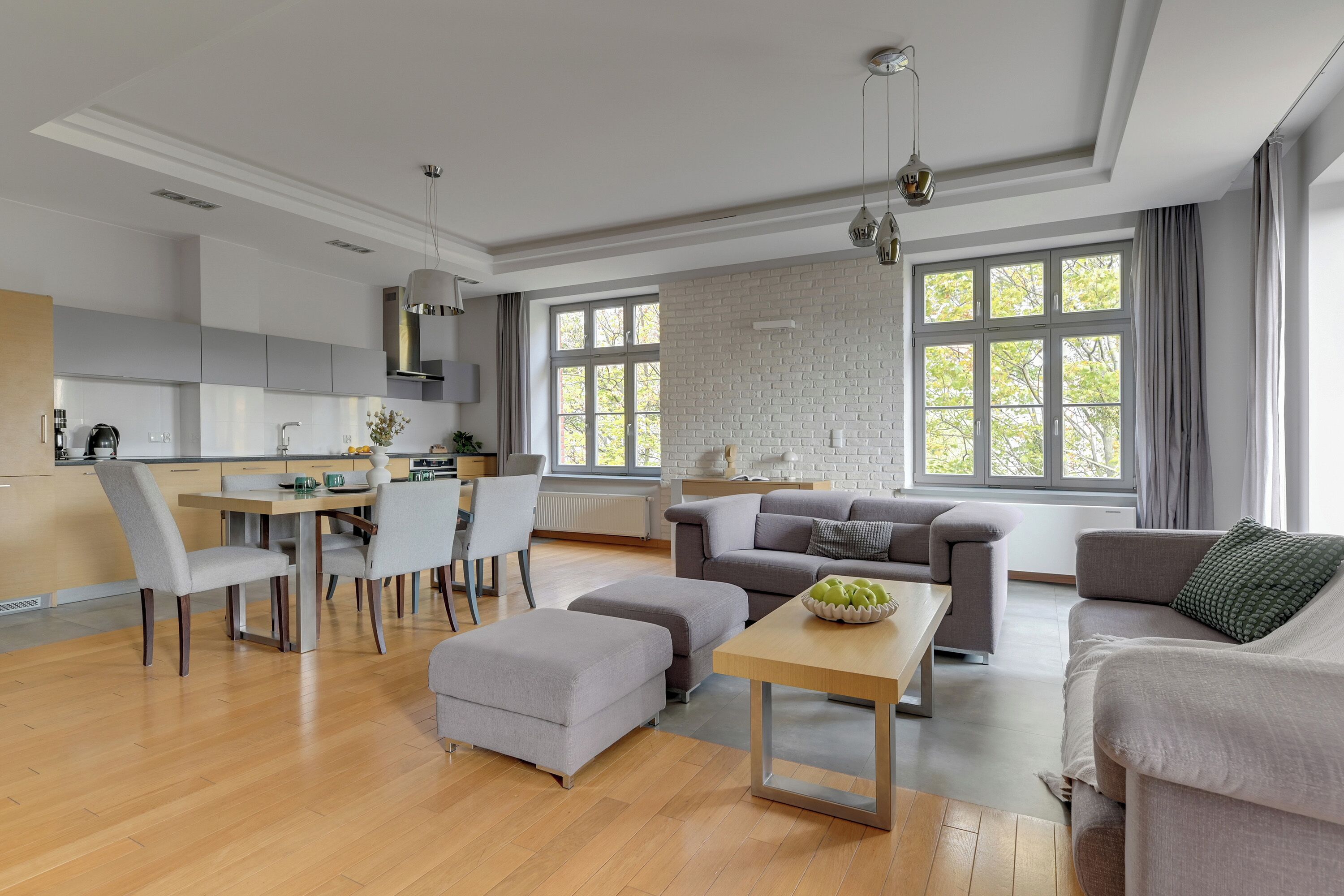 Ein modernes Wohnzimmer mit Essbereich, grauen Sofas und einem Holztisch.