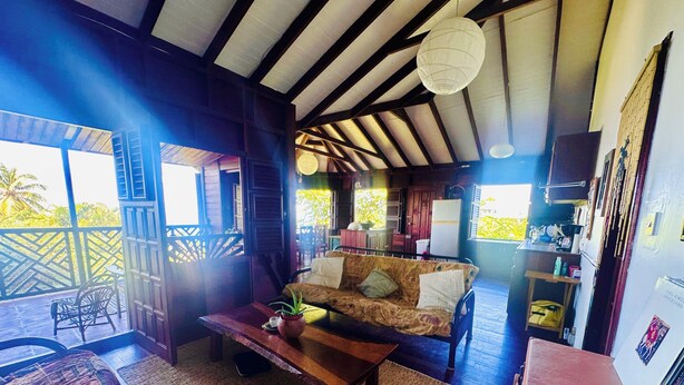A cozy room with a wooden ceiling, a sofa with cushions, a coffee table, and a dining area with chairs. - Modest family home located in a quiet neighbourhood on Calibishie Ridge. (Calibishie)