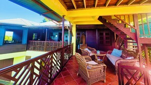 A covered outdoor area with wicker furniture, a wooden staircase, and a view of the building's exterior. - Modest family home located in a quiet neighbourhood on Calibishie Ridge. (Calibishie)