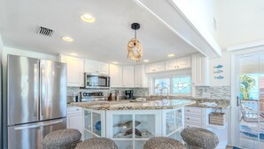Een moderne keuken met witte kasten, roestvrijstalen apparatuur en een centraal eiland met barstoelen.