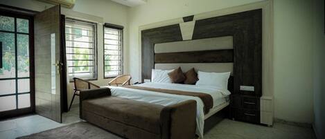 A bedroom with a bed, a chair, a bedside table, a nightstand, and a window.