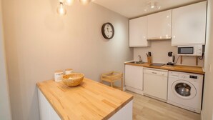 Eine kleine Küche mit einer Holzausziehtafel, einer Waschmaschine, einer Mikrowelle und einer Wanduhr.