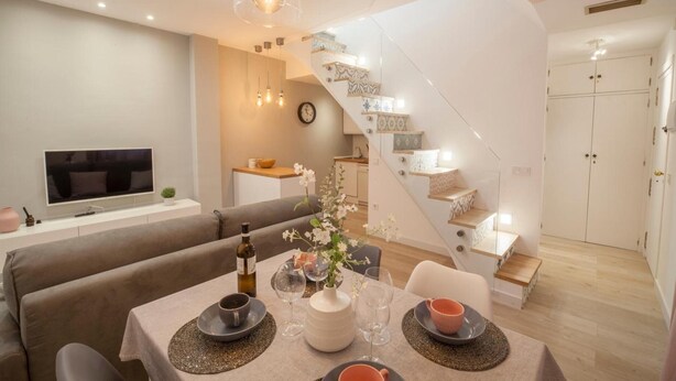 Ein modernes Wohnzimmer mit Essbereich, einer Treppe und einem Fernseher an der Wand.