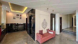 Eine großzügige Lobby mit einem roten Sofa, einem schwarzen Empfangstresen und einer dekorativen Wandarbeit.