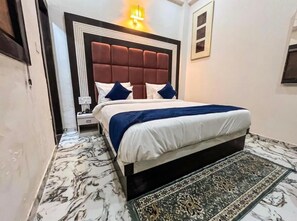 A bedroom with a large bed, a headboard, a nightstand, and a patterned rug. - Hotel Atlantiis Suites by Signature Stay (Agra)