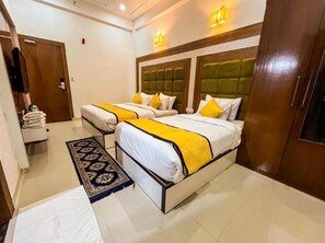 A hotel room with two beds, each with white bedding and yellow accents, a wooden headboard, a small rug, and a wardrobe. - Hotel Atlantiis Suites by Signature Stay (Agra)