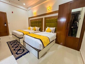 A hotel room with two beds, each with a yellow and white bedspread, a large mirror, and a wooden wardrobe. - Hotel Atlantiis Suites by Signature Stay (Agra)